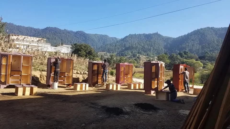 Artesanos de Mueblería Jenny Yax trabajando en roperos de madera con las montañas de Sololá al fondo